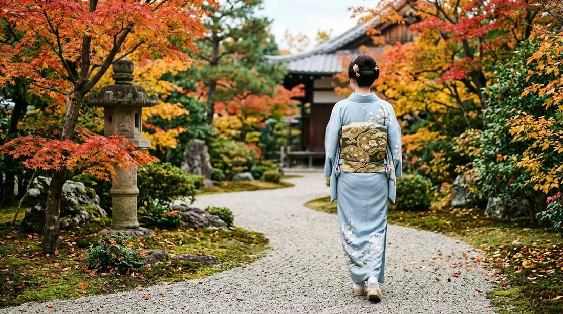 Femme en kimono de soie bleu pâle et obi brodé marchant dans un jardin de temple japonais en automne
